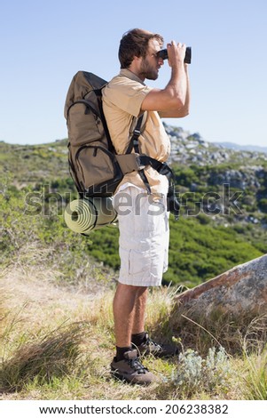 Handsome hiker looking through binoculars on a sunny day
