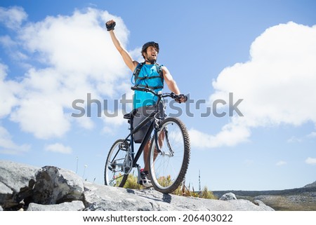 Fit man cycling on rocky terrain and cheering on a sunny day