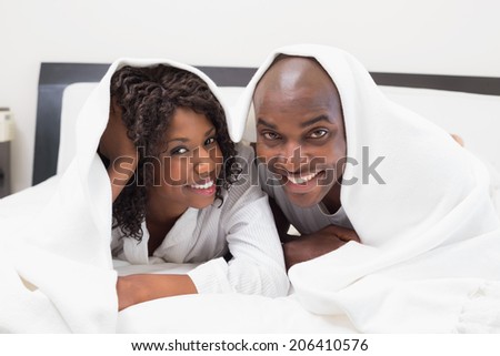 Happy couple lying on bed together under the duvet at home in the bedroom