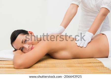 Beautiful brunette enjoying an exfoliating back massage smiling at camera in the health spa