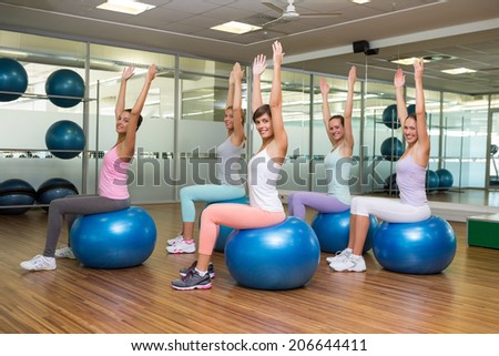 Fitness class sitting on exercise balls in studio at the gym