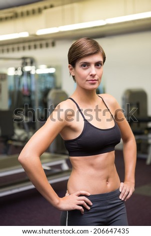 Fit brunette in black sports bra looking at camera at the gym