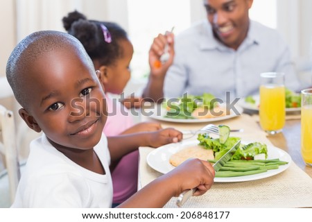Family enjoying a healthy meal together with son smiling at camera at home in the kitchen