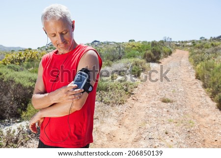 Fit man changing the song on his music player on mountain trail on a sunny day