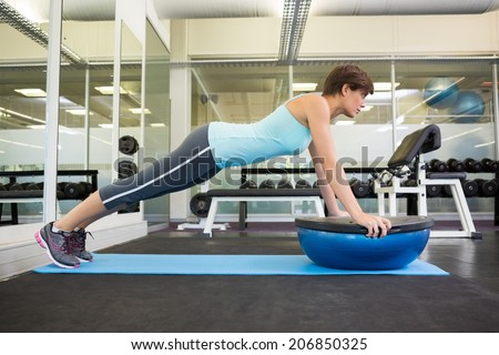 Fit brunette using bosu ball in plank position at the gym