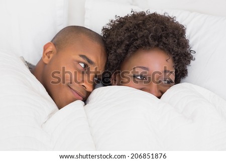 Happy couple lying in bed under the duvet at home in the bedroom