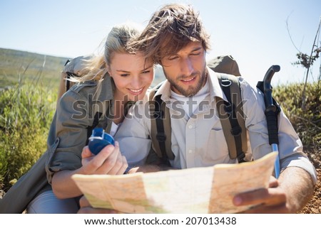 Hiking couple taking a break on mountain terrain using map and compass on a sunny day