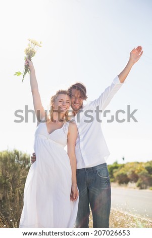 Attractive couple standing with arms raised by the road on a sunny day