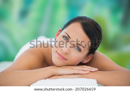 Beautiful brunette relaxing on massage table smiling at camera at a luxury spa