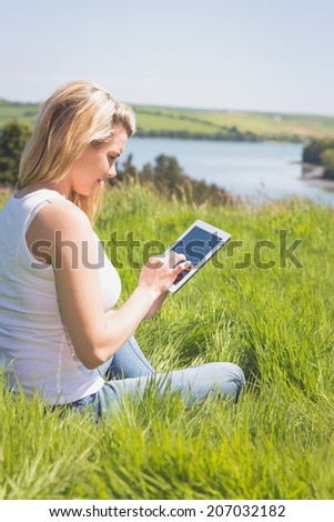 Pretty blonde sitting on grass using her tablet on a sunny day in the countryside