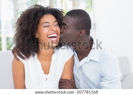 Attractive man kissing his girlfriend on the cheek at home in the living room
