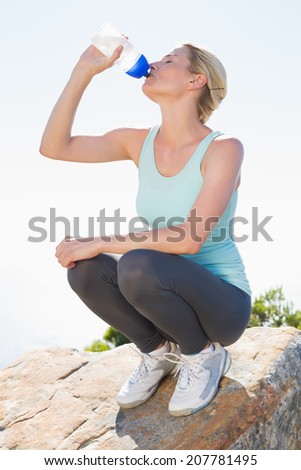 Fit blonde sitting at summit drinking from water bottle on a sunny day