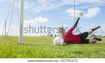 Goalkeeper in red making a save on a clear day