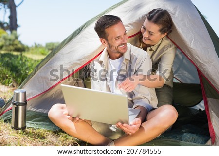 Outdoorsy couple looking at the laptop outside tent on a sunny day