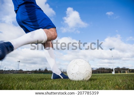 Football player in blue about to kick ball on a clear day
