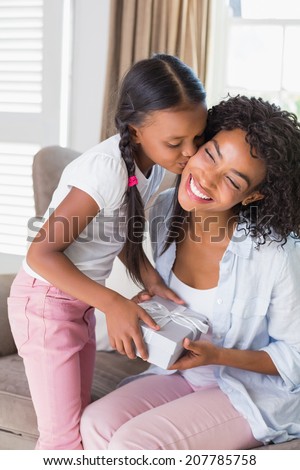 Pretty mother sitting on couch offering daughter a gift at home in the living room