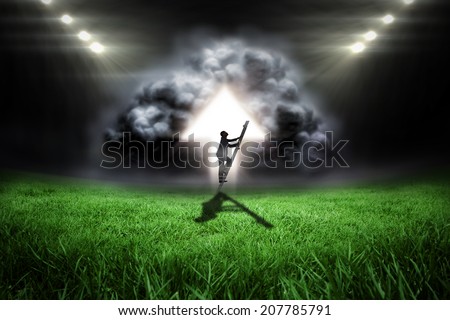 Businessman climbing up ladder against football pitch with bright lights