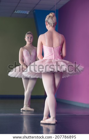 Graceful ballerina standing in first position in front of mirror in the ballet studio