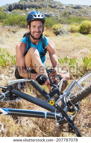 Fit cyclist tying his shoelace on mountain trail smiling at camera on a sunny day