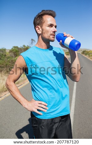 Athletic man on open road taking a drink on a sunny day