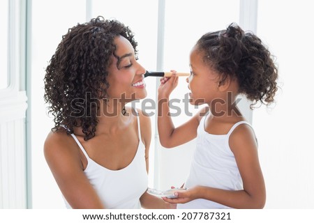 Cute daughter putting makeup on her mothers face at home in the bathroom