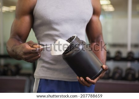 Mid section of a body builder holding a scoop of protein mix in gym