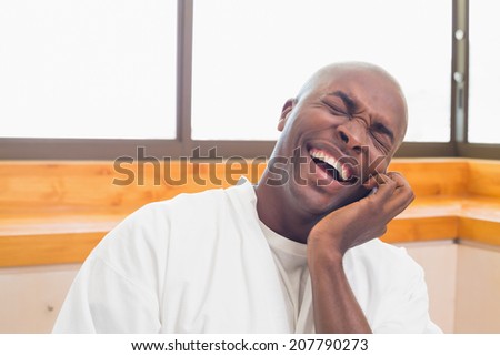 Laughing man in bathrobe talking on phone at home in the kitchen