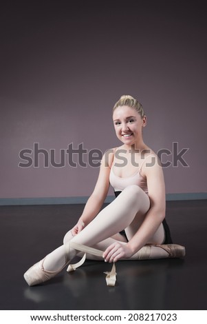 Pretty ballerina tying the ribbon on her ballet slippers in the ballet studio