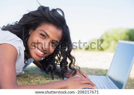 Casual pretty woman lying on the grass using her laptop on a sunny day in the countryside