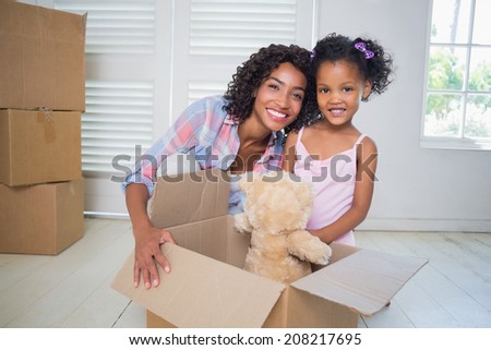 Cute daughter unpacking her teddy bear with mother in their new home