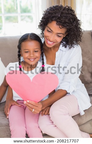 Pretty mother sitting on couch with daughter reading heart card at home in the living room