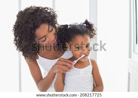 Pretty mother helping her daughter brush her teeth at home in the bathroom