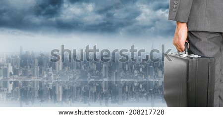 Businessman holding briefcase against room with large window looking on city