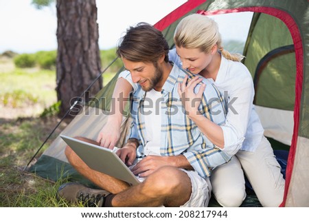 Attractive couple sitting by their tent using laptop on a sunny day