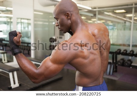 Side view of a shirtless muscular boxer in defensive stance in health club