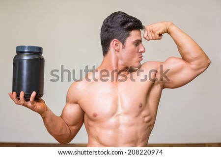 Portrait of a muscular man posing with nutritional supplement in gym