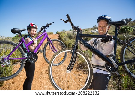 Active couple carrying their bikes on country terrain together on a sunny day