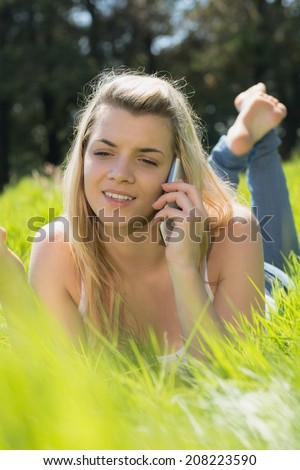 Pretty blonde lying on grass talking on phone on a sunny day in the countryside