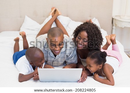 Happy family using laptop together on bed at home in the bedroom