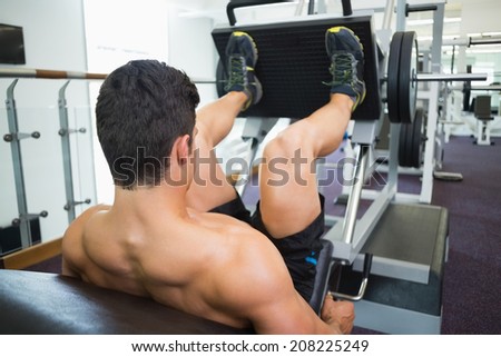 Rear view of male weightlifter doing leg presses in gym