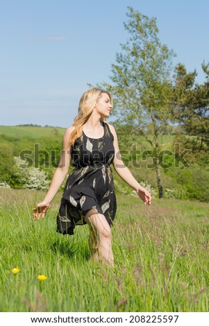 Pretty blonde in sundress walking through field on a sunny day in the countryside