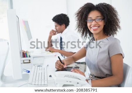 Young pretty designer smiling at camera at her desk in her office