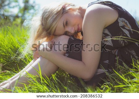 Pretty blonde in sundress sitting on grass on a sunny day in the countryside