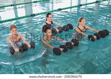 Female fitness class doing aqua aerobics with foam dumbbells in swimming pool at the leisure centre