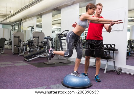 Personal trainer with client on bosu ball at the gym