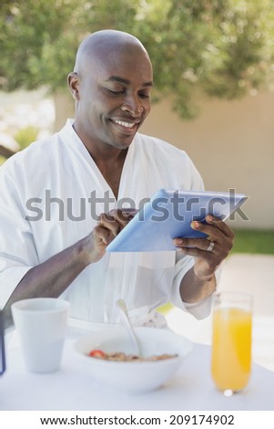 Handsome man in bathrobe using tablet at breakfast outside on a sunny day