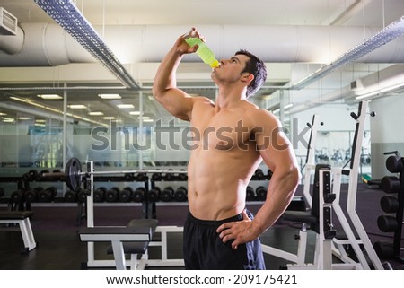 Side view of a shirtless muscular man drinking energy drink in gym