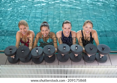 Female fitness class doing aqua aerobics with foam dumbbells in swimming pool at the leisure centre