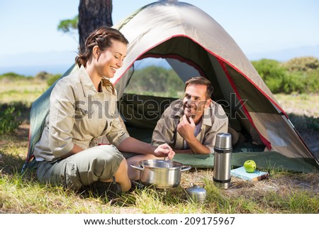 Outdoorsy couple cooking on camping stove outside tent on a sunny day