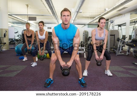 Muscular instructor leading kettlebell class at the gym